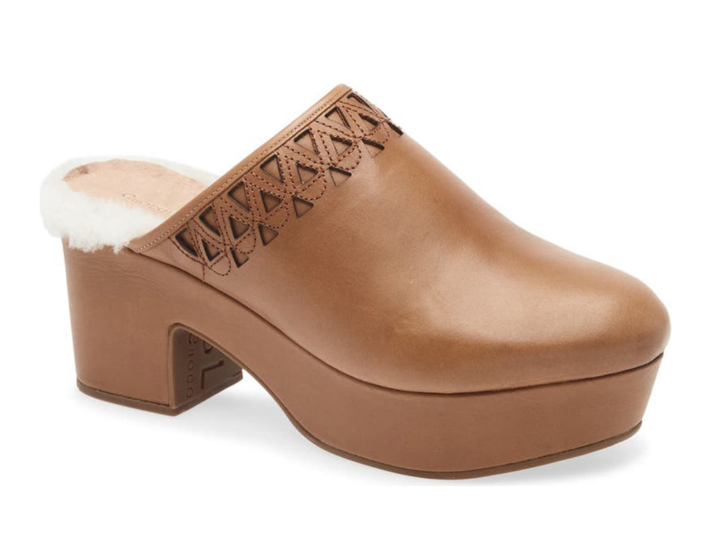 Brown heeled clog shoe with decorative cutout on upper and fur trim mid sole on a white background side angle view