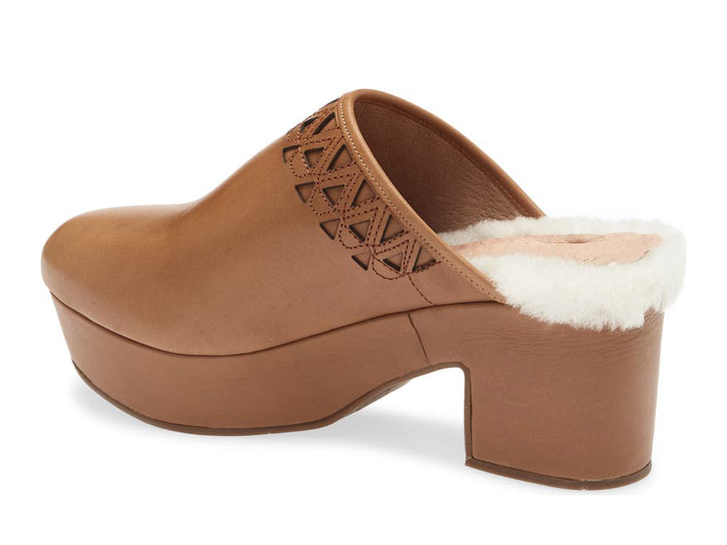 Brown heeled clog shoe with decorative cutout on upper and fur trim mid sole on a white background side angle view