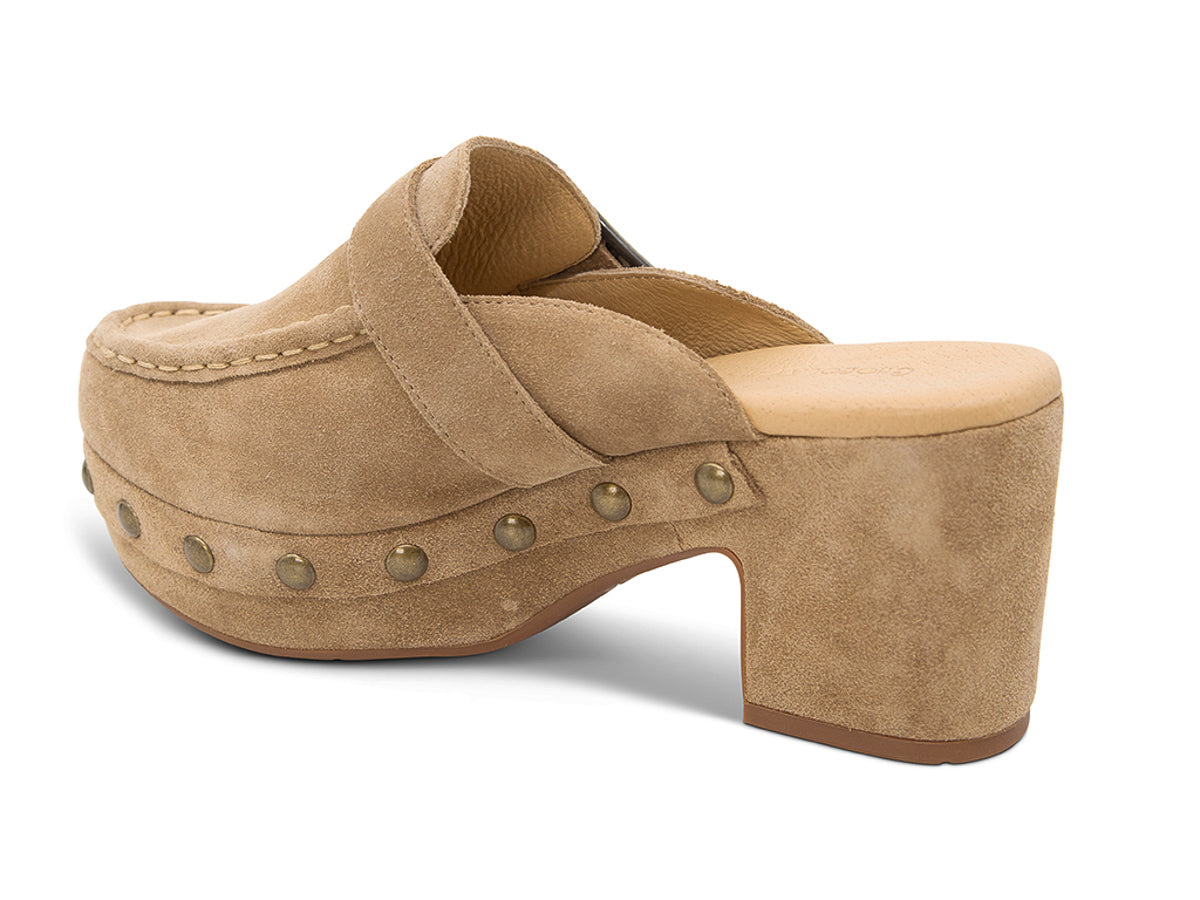 Camel suede slide in block heel clog shoe with a decorative strap buckle and grommet studson a white background side angle view 
