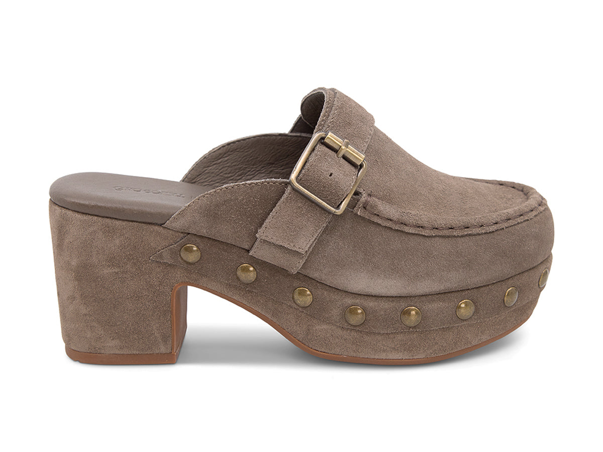 Taupe suede slide in block heel clog shoe with a decorative strap buckle and grommet studson a white background side view 