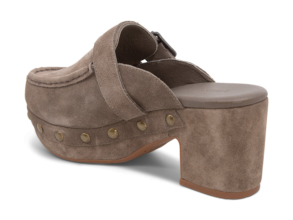 Taupe suede slide in block heel clog shoe with a decorative strap buckle and grommet studson a white background side angle view 