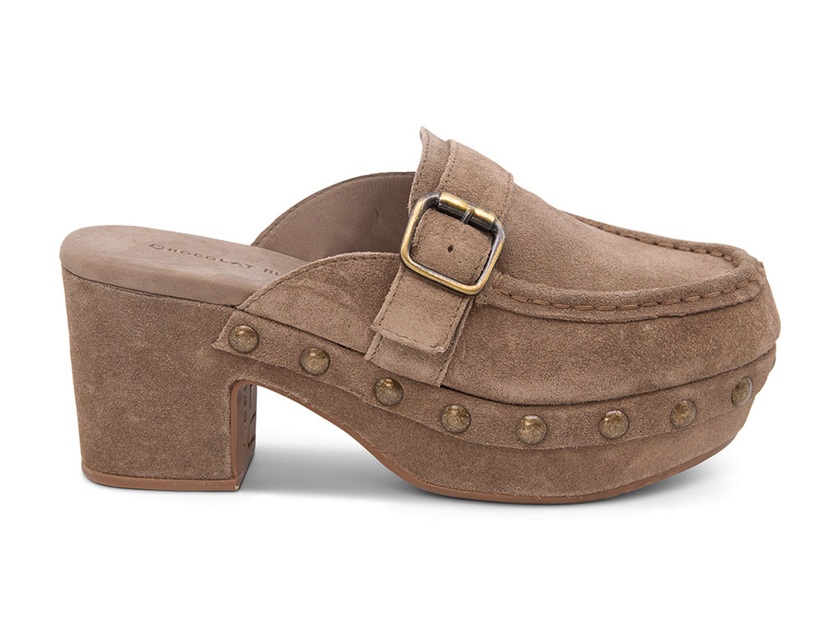Toffee suede slide in block heel clog shoe with a decorative strap buckle and grommet studson a white background side  view 