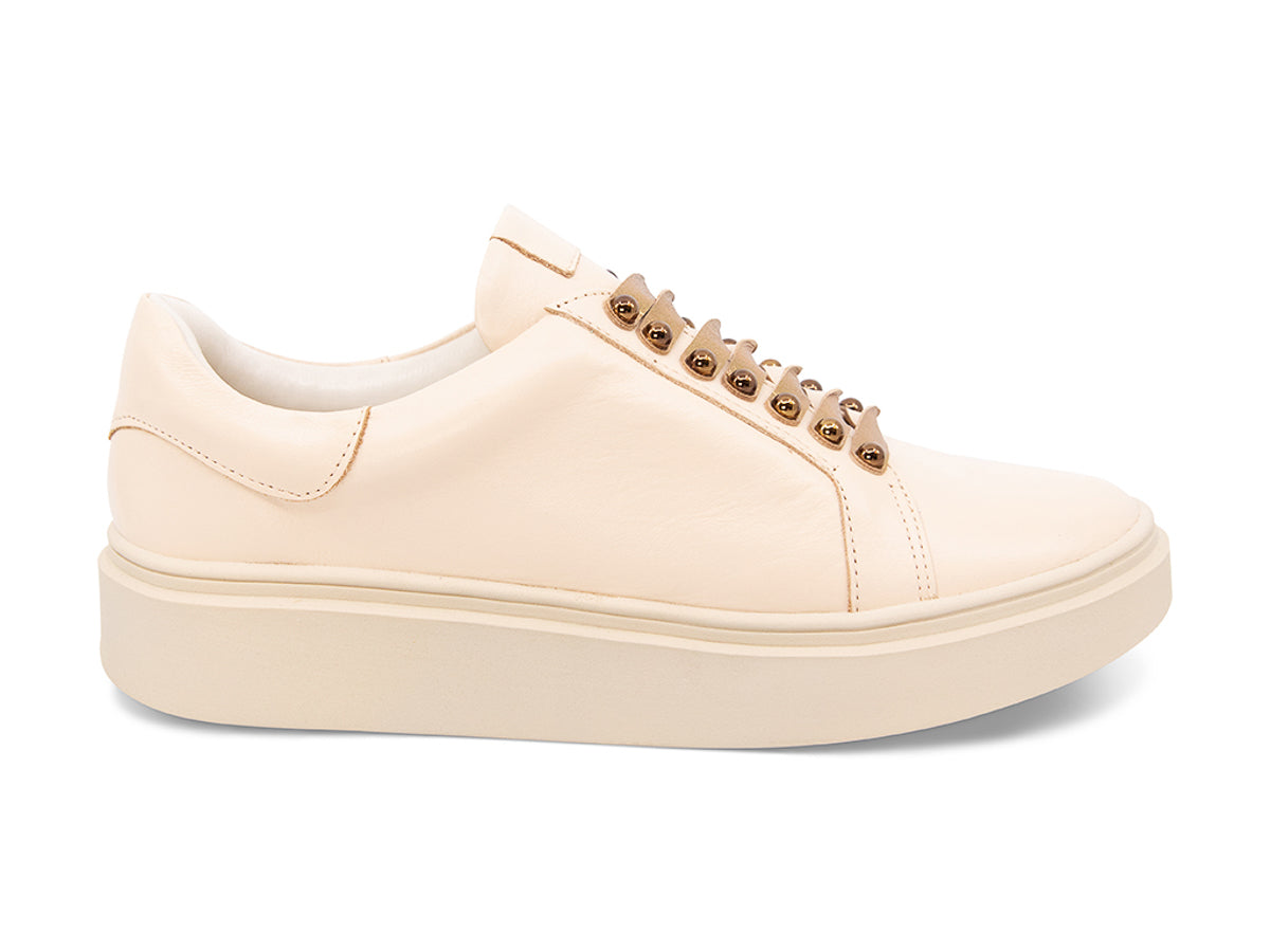 Beige sneaker with gold laces and studs on laces on a white background side view