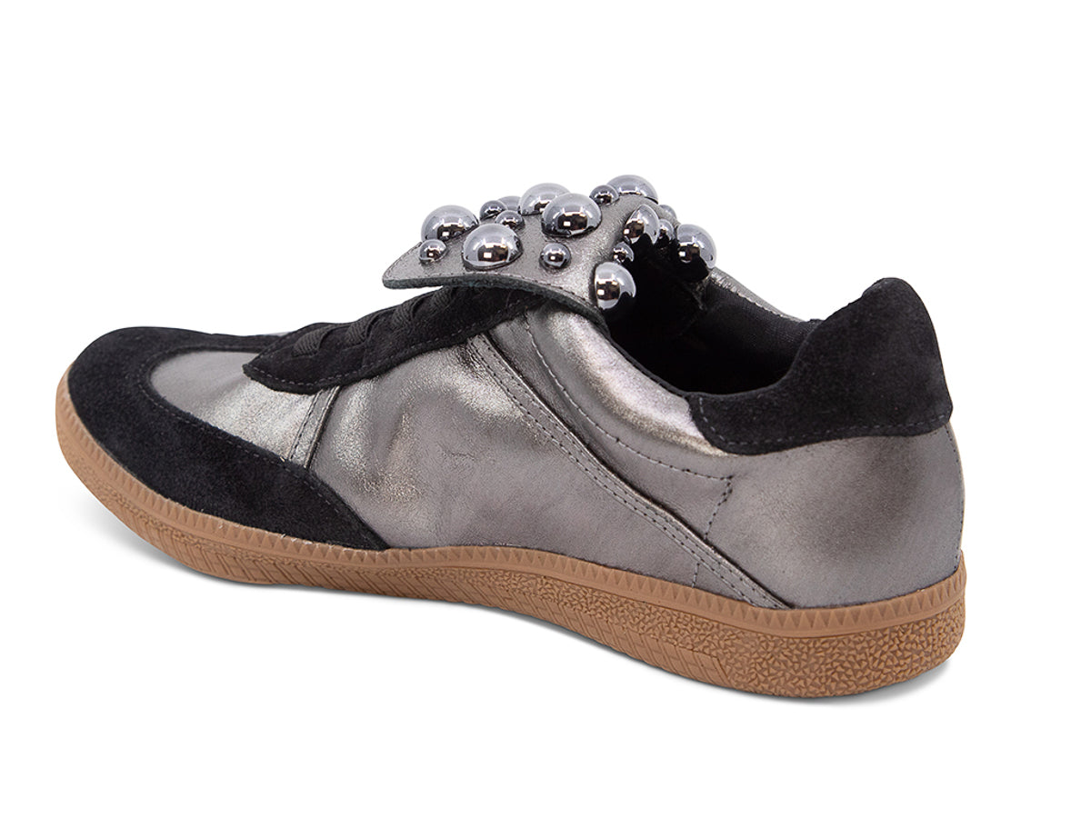 Silver and black sneaker with decorative stud embellishments and brown sole on a white background side angle view