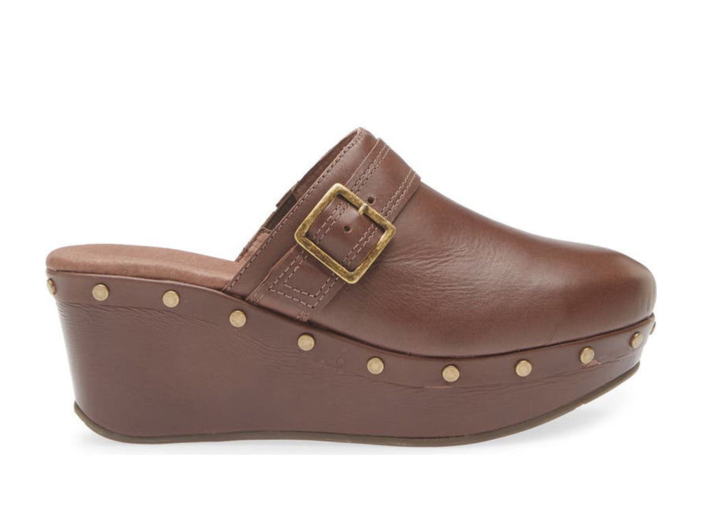 Brown leather slide in clog wedge platform shoe with top strap and buckle decoration and grommet studs on a white background side view