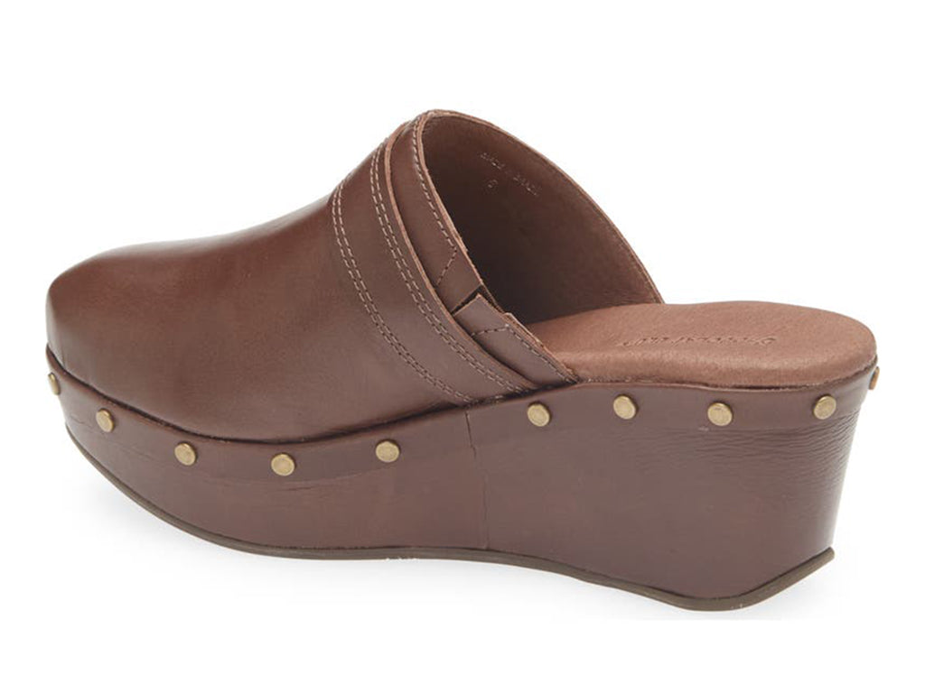 Brown leather slide in clog wedge platform shoe with top strap and buckle decoration and grommet studs on a white background side angle view