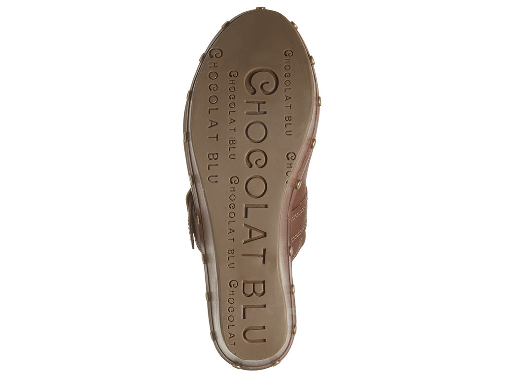 Brown leather slide in clog wedge platform shoe with top strap and buckle decoration and grommet studs on a white background bottom sole view